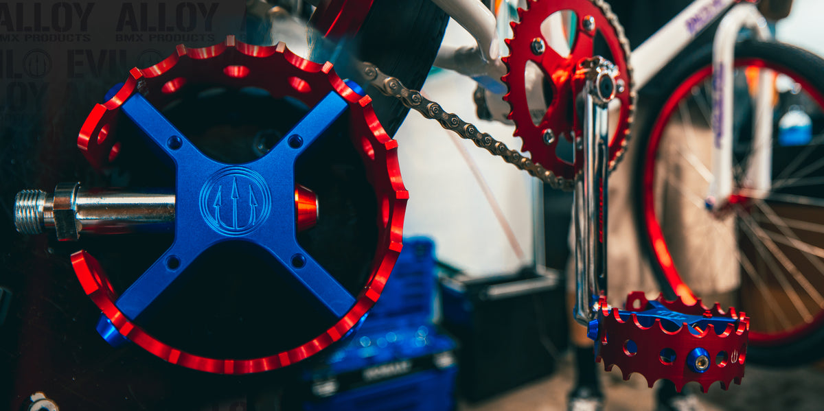 Blue Evil Alloy pedal bodies with red cages beside a custom bike drivetrain